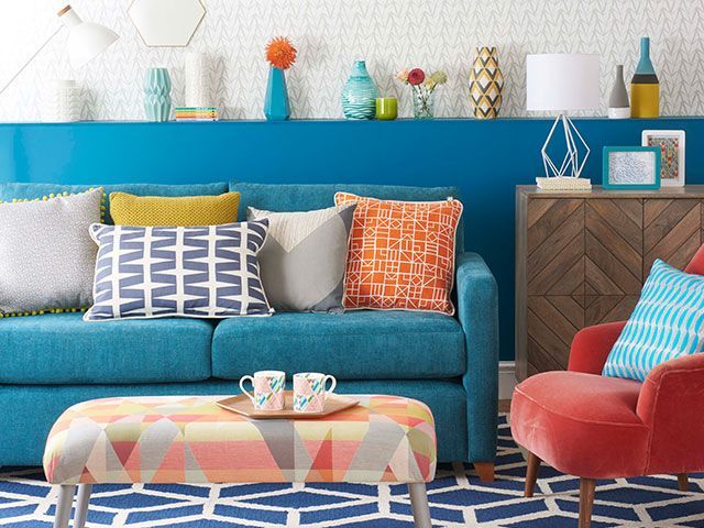 一个现代客厅里的蓝色沙发，一个几何脚凳，有图案的靠垫，还有一个半墙的搁板