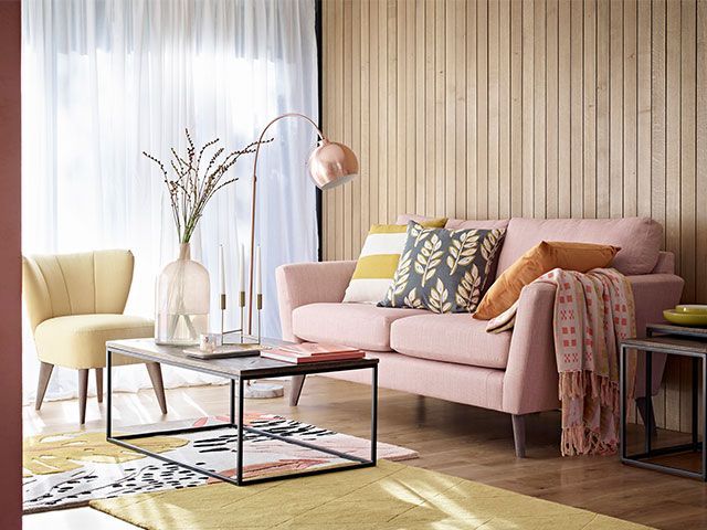 一间带有木质镶板的斯堪迪风格的客厅，一张千禧年风格的粉色沙发，一张黄色地毯和铜质装饰