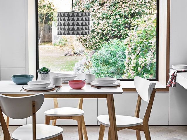 一个斯堪的纳维亚风格的白色用餐区，通过一个大落地窗可以看到花园