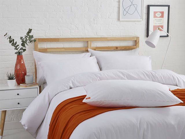 一间白色砖卧室的图片有一个nanu床与白色床上用品和橙色投掷 -  ananu-bedroom-goodhomesmagazine.com