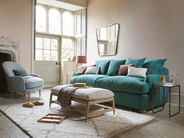 蓝绿色沙发床，散落的靠垫和凳子，松软的奶油色地毯，goodhomesmagazine.com