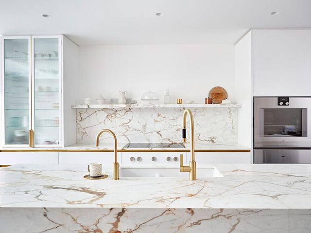 白色厨房与声明的石头表面和黄铜细节- goodhomesmagazine.com