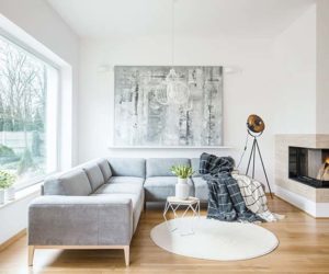 白色地毯旁边​​的灰色角落长沙发在客厅内部与壁炉和绘画