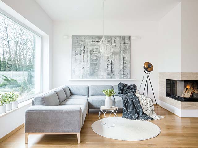 白色地毯旁边的灰色角落沙发在客厅内部的壁炉和绘画