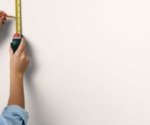 一个女人的手用铅笔和卷尺在墙上做记号-涂过的床头板- Goodhomesmagazine.com