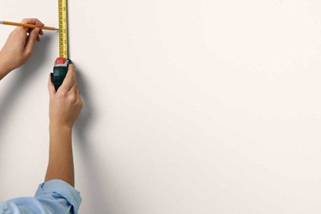 女人的手用铅笔和卷尺在墙上做记号——画在床头板上——Goodhomesmagazine.com