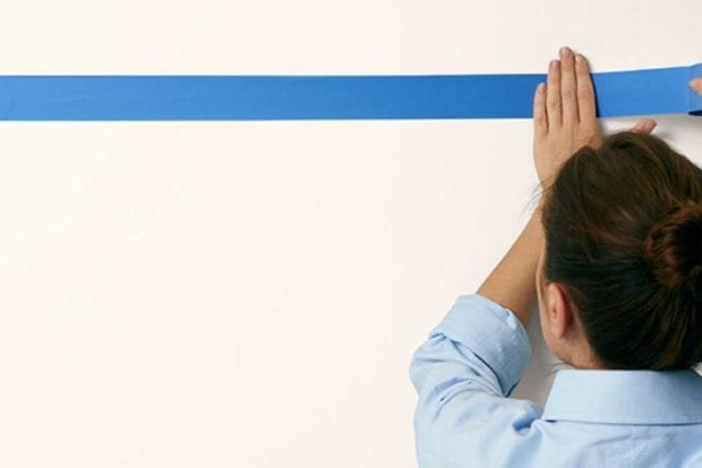 女人在墙上用蓝色胶带标记出一条线——画过的床头板——Goodhomesmagazine.com