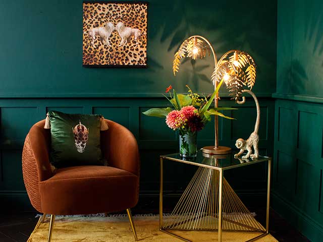 一间翠绿房间的角落里有一把烧焦的橙色天鹅绒扶手椅，旁边是一张金色的边桌，上面装饰着装饰品-泥土色调-Goodhomesmagazine.com