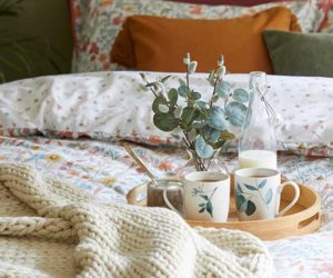 一张床上放着传统图案的床上用品，一个放着马克杯的木托盘，一个编织的垫子和一个烧焦的橙色靠垫——Goodhomesmagazine.com
