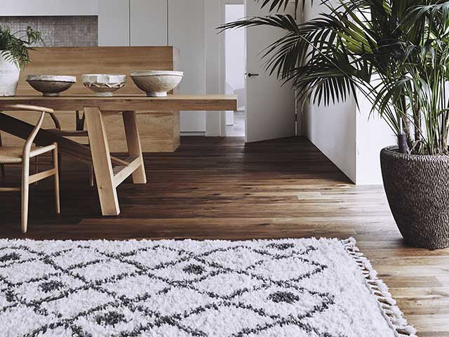 深棕色木质地板上有黑色阿兹特克印花的白色绒毛地毯- 2021年地板趋势- Goodhomesmagazine.com