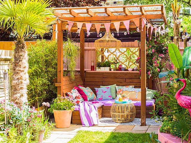一个长满草的花园，凉棚被装饰着彩旗、靠垫和毯子-花园派对的必需品- Goodhomesmagazine.com
