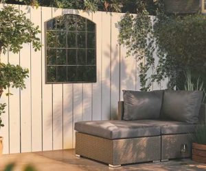 灰色的藤沙发在白色镶板栅栏前，上面挂着一面哥特式的镜子——花园镜子——Goodhomesmagazine.com