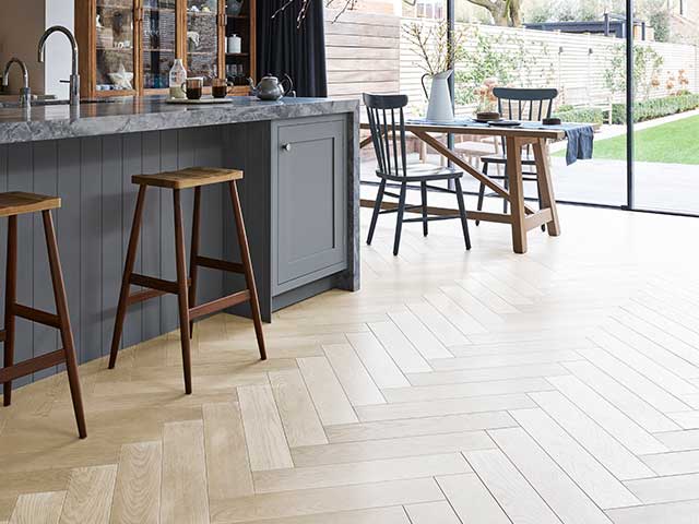 人字形图案的轻木地板在厨房，有一个早餐酒吧和木制桌子。地板趋势- Goodhomesmagazine.com