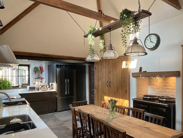 modern rustic kitchen with sleek dark units, farmhouse table, wooden chairs and oversize industrial pendant lights