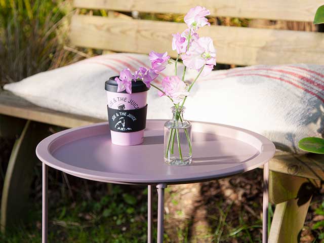 一个木凳和靠垫和腮红粉红色金属托盘桌在它面前显示花瓶和咖啡杯 -  2021庭院家具 -  Goodhomesmagazine.com