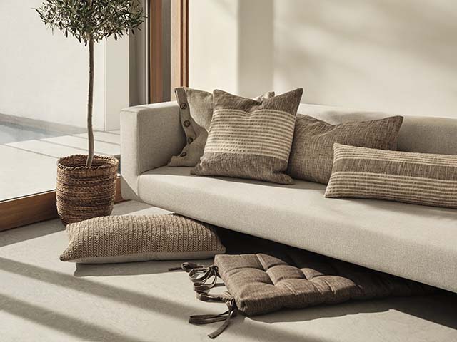 手工制作的棕色靠垫，自然颜色的沙发上有室内植物，goodhomesmagazine.com