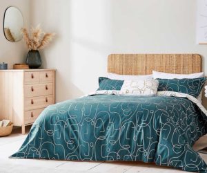 一间卧室，有一个编织的木制床头板和一套蓝绿色的床上用品，上面有抽象面孔的单线连续图案
