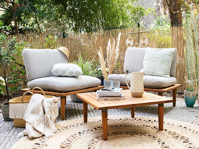 圆形编织的自然极简户外地毯，木制咖啡桌和带灰色靠垫的背靠背椅子