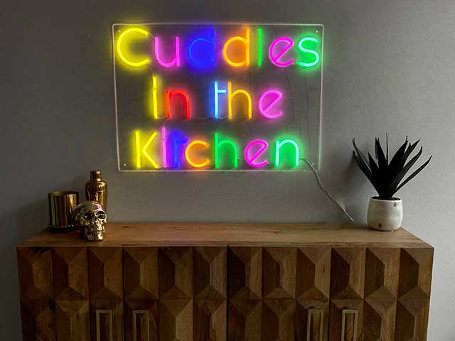 在一张边桌上方，五颜六色的“厨房里的拥抱”霓虹灯