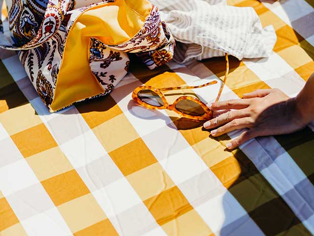 女孩坐在黄色条纹的毯子太阳镜和生态手提包